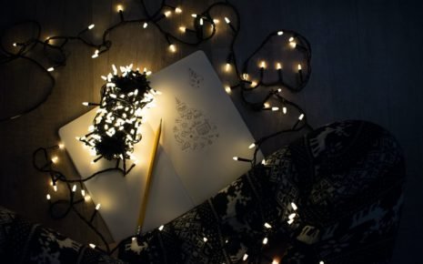 A notebook surrounded by Christmas lights on the floor in front of a person’s legs