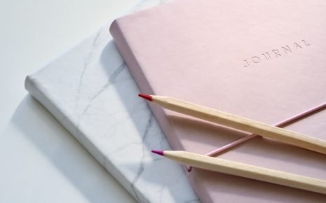 Pink and marble journals with red and purple coloring pencils sitting on top of them